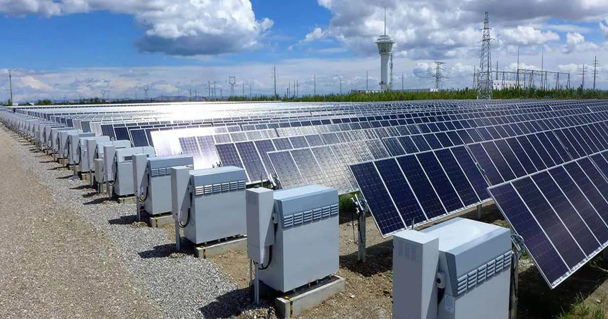 Usina solar fotovoltaica com fileiras de inversores e subestação ao fundo